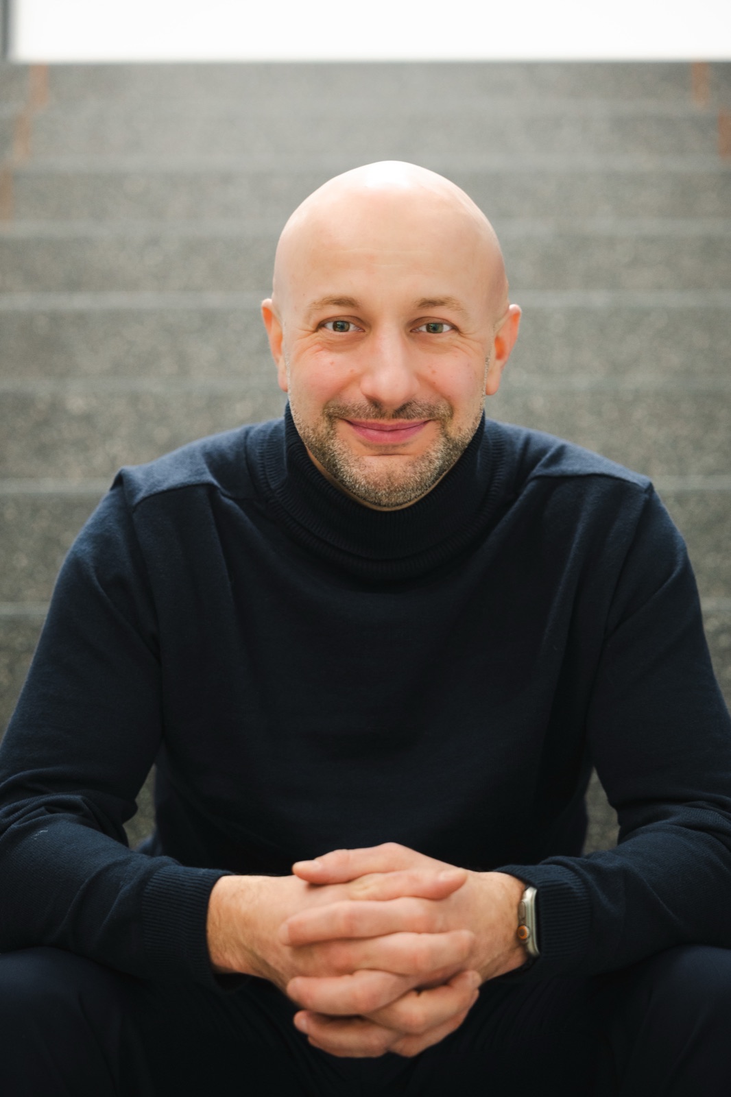 Hubert Gęsiarz siedzi na schodach, w granatowym golfie, uśmiecha się do obiektywu