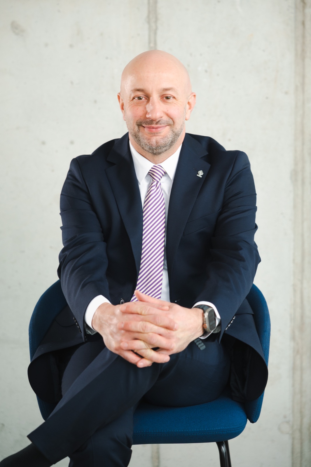 Hubert Gęsiarz w garniturze siedzi na niebieskim krześle, dłonie splecione na kolanie
